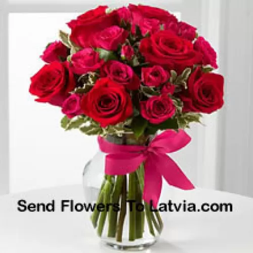 季節の詰め物入りの19本の赤いバラがガラスの花瓶に入れられ、ピンクのリボンで飾られています